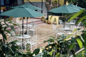 An outdoor patio area with white metal chairs and tables, green umbrellas, and potted plants. - The Fern Hillside Resort Bhimtal (Nainital)