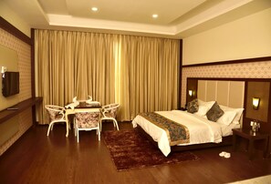 A hotel room with a large bed, a desk with chairs, a television, and a large window with curtains. - The Fern Hillside Resort Bhimtal (Nainital)