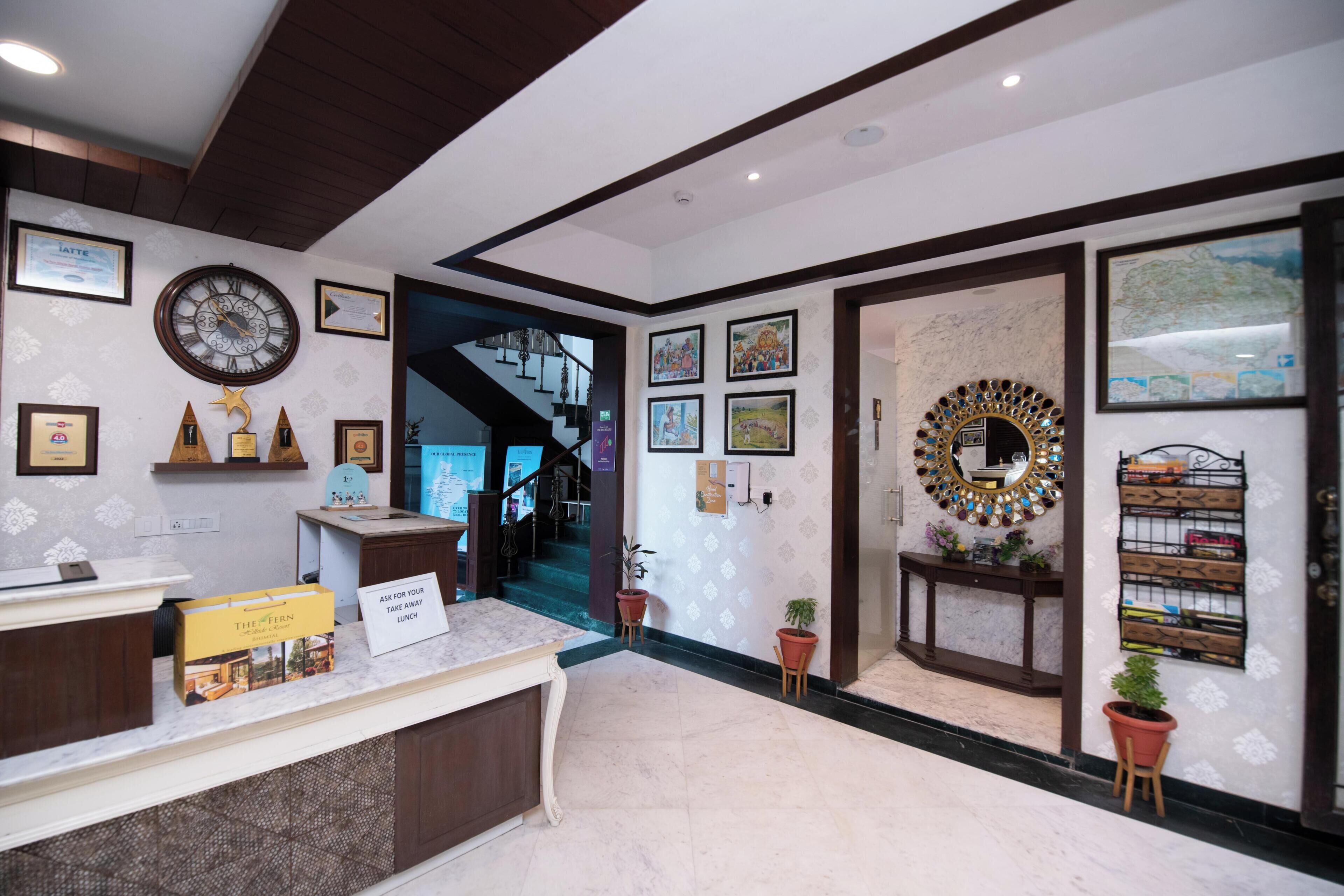 Un espace d’accueil d’hôtel avec un comptoir en marbre, des certificats encadrés, une horloge et un escalier menant aux étages supérieurs.