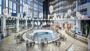 Eine geräumige Lobby mit einer zentralen, runden Sitzgruppe, großen Fenstern und modernen Kronleuchtern.