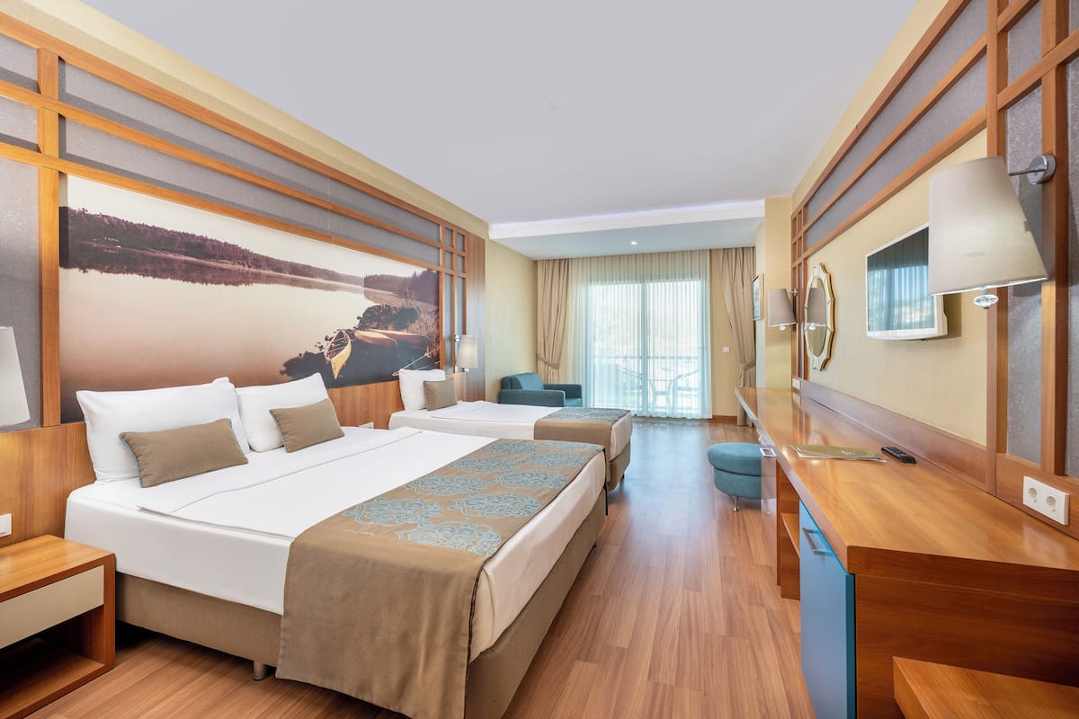 A hotel room with two beds, a desk, a chair, and a large window with curtains.