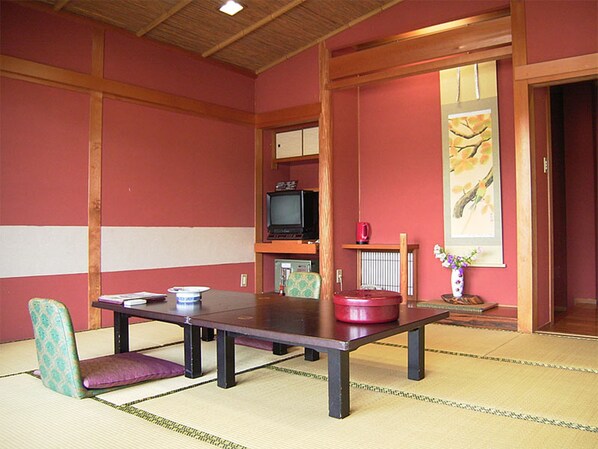 Una habitación con esteras de tatami, una mesa baja, dos sillas, un televisor y un cuadro en la pared.