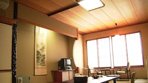 Une pièce de style japonais traditionnel, avec un sol recouvert de tatamis, une table basse, des chaises, un téléviseur et une grande fenêtre.
