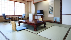 Une pièce de style japonais traditionnel, avec un sol recouvert de tatamis, une basse table en bois, deux chaises bleues, un téléviseur et un tableau accroché au mur.