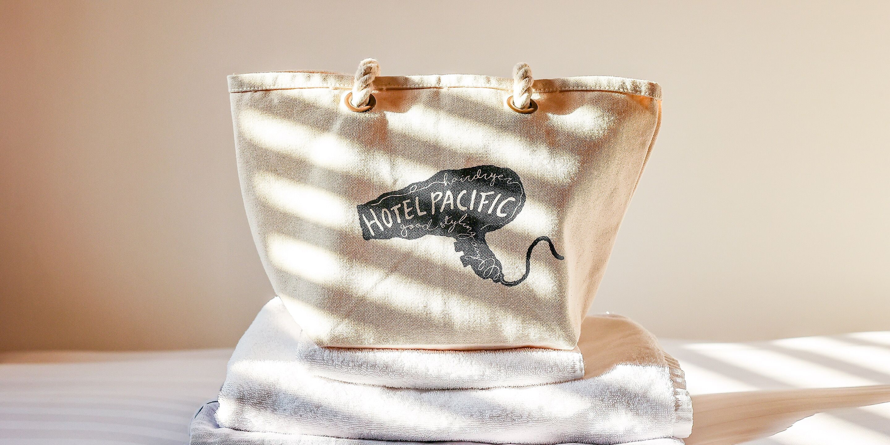 A canvas tote bag with a black embroidered design and the text "HOTEL PACIFIC."