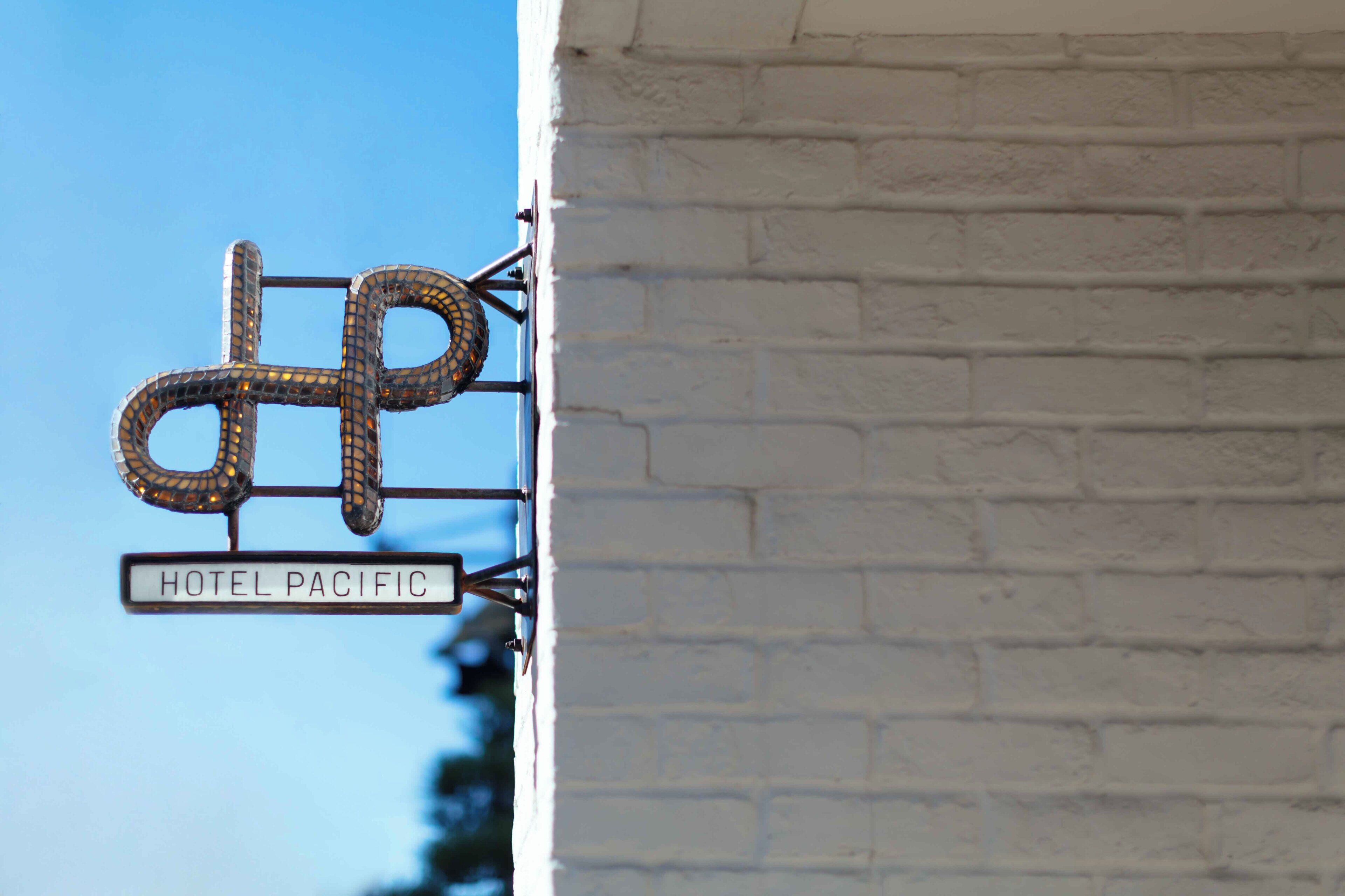 A hotel sign with a unique design, attached to a white brick wall.
