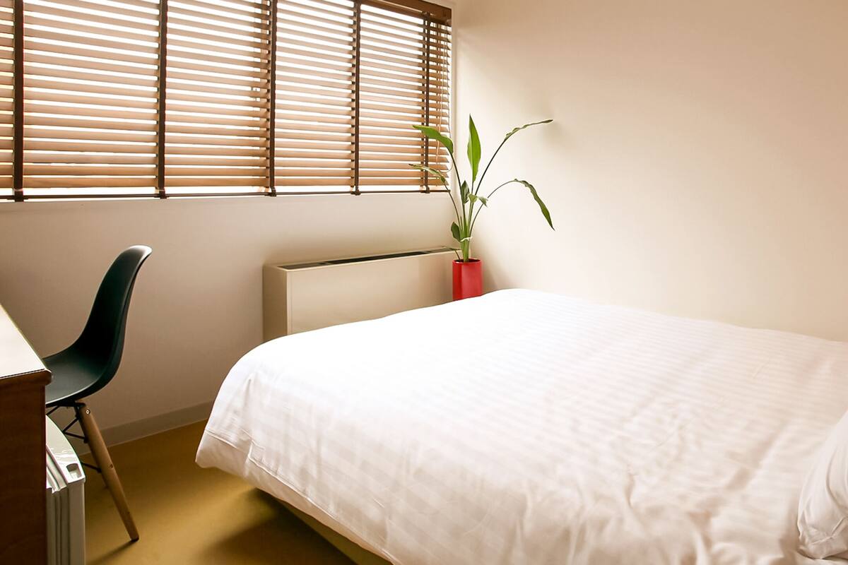 A neatly arranged bedroom with a bed, a chair, a radiator, a potted plant, and a bedside table.