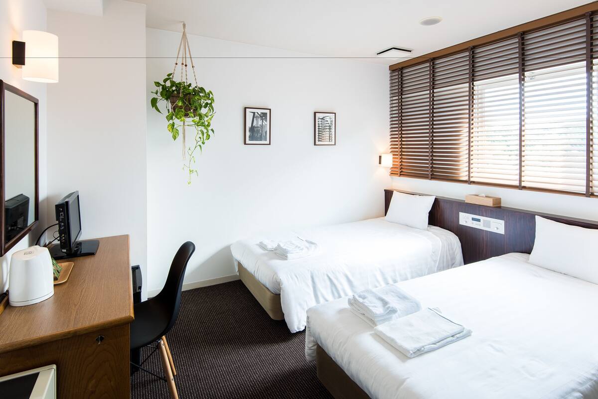 A hotel room with two beds, a desk with a computer, a chair, a hanging plant, and framed pictures on the wall.