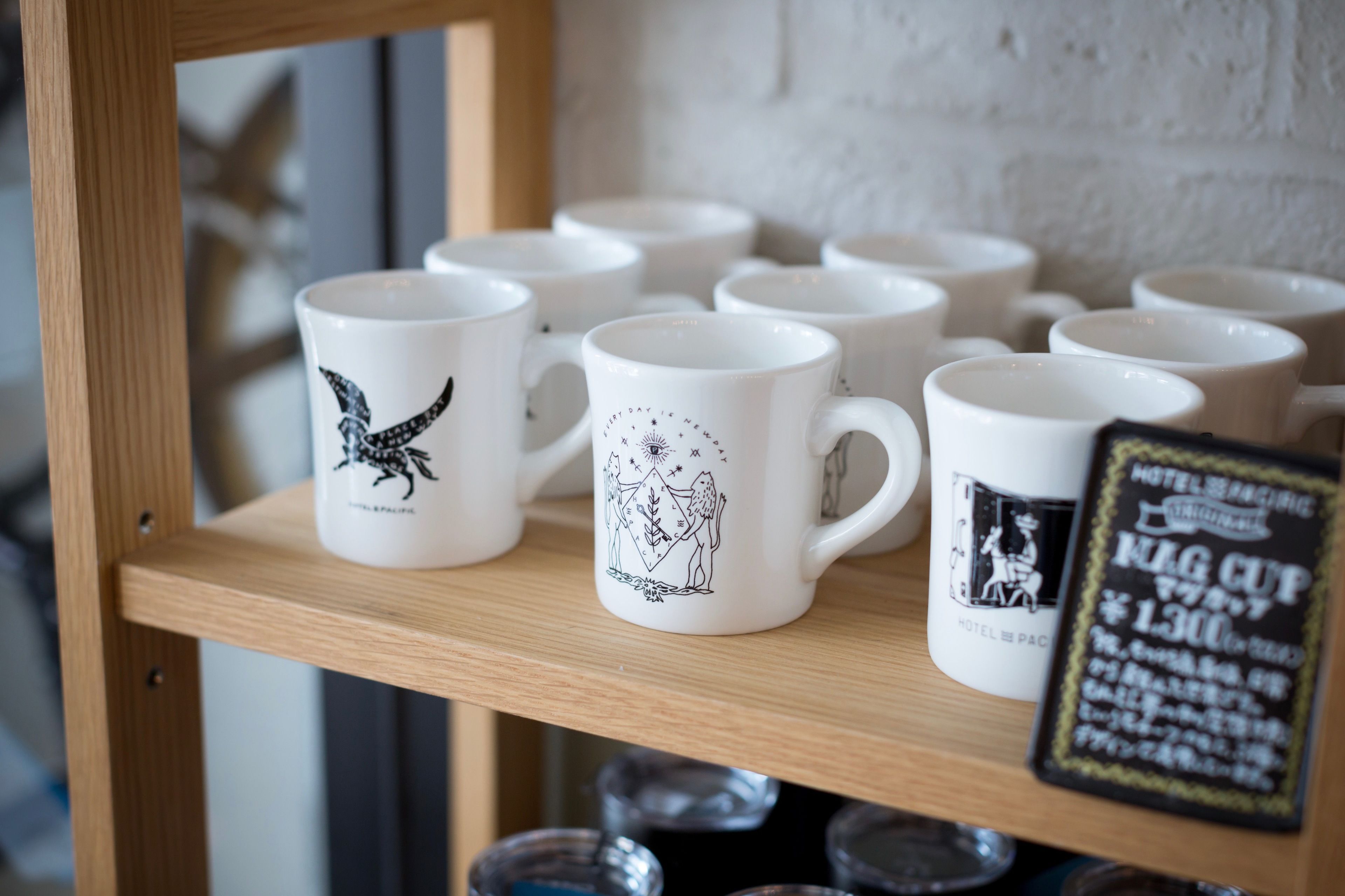 A display of white mugs with black designs on a wooden shelf.