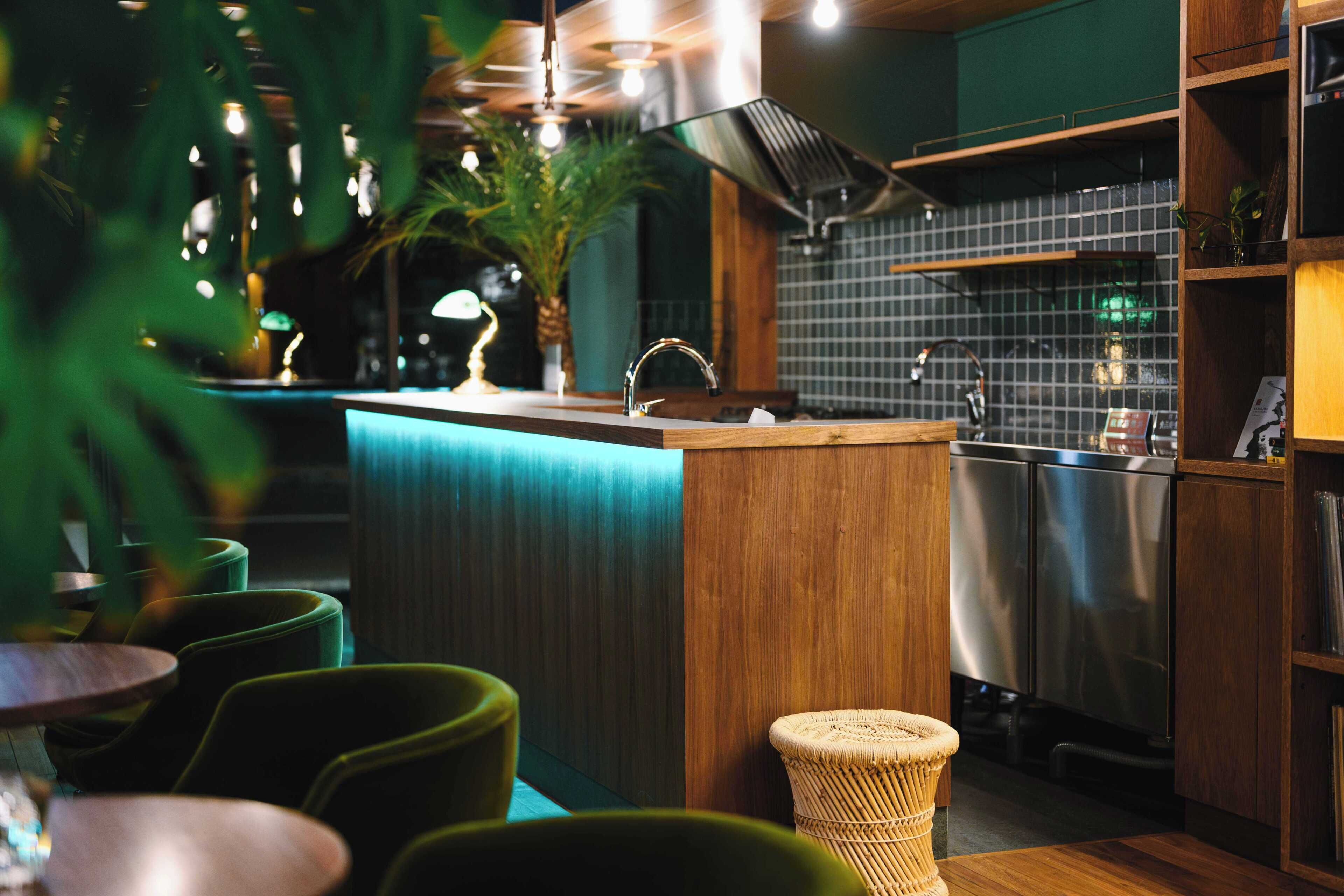 Une cuisine moderne avec un comptoir-bar en bois, des appareils électroménagers en acier inoxydable et des chaises vertes.