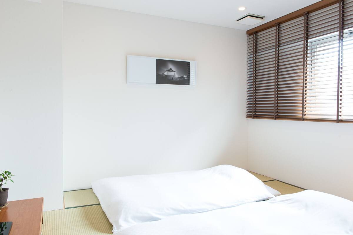 A minimalist hotel room with a bed, a small table with a plant, and a picture on the wall.