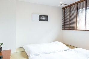 A minimalist hotel room with a bed, a small table with a plant, and a picture on the wall. - Hotel Pacific Kanazawa (Kanazawa)