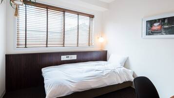 Habitación de hotel con cama, cabecero, luz fijada en la pared, ventana con persianas y un cuadro en la pared.