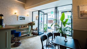 A cafe with a brick wall, wooden bar, blue bar stools, and a large window with a view of the street. - Hotel Pacific Kanazawa (Kanazawa)