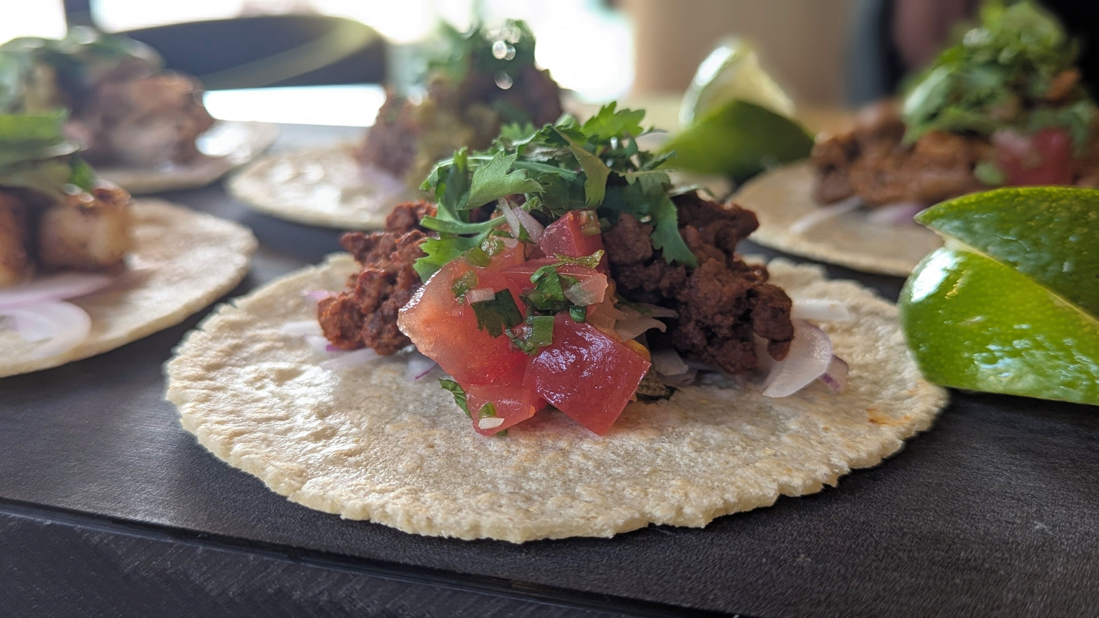 A table with food items, specifically tacos with meat, tomatoes, and onions.