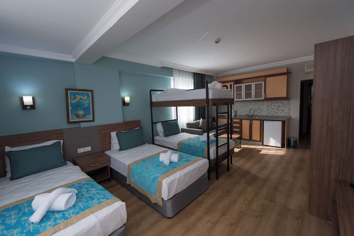 Quarto de hotel com três camas, uma kitchenette e um banheiro.