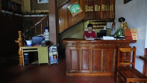 A reception desk at Nganningg Bac Ha Hotel with a wooden design, a computer, and a sign indicating a reception area.