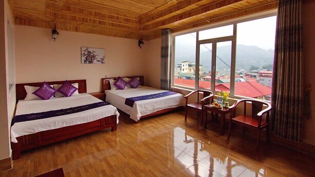 A hotel room with two wooden beds, a wooden ceiling, a large window with a view of buildings and mountains, and a small table with chairs.