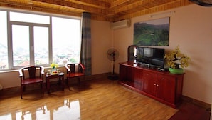 A living room with wooden flooring, a television on a cabinet, a fan, and a window with a view of a landscape.