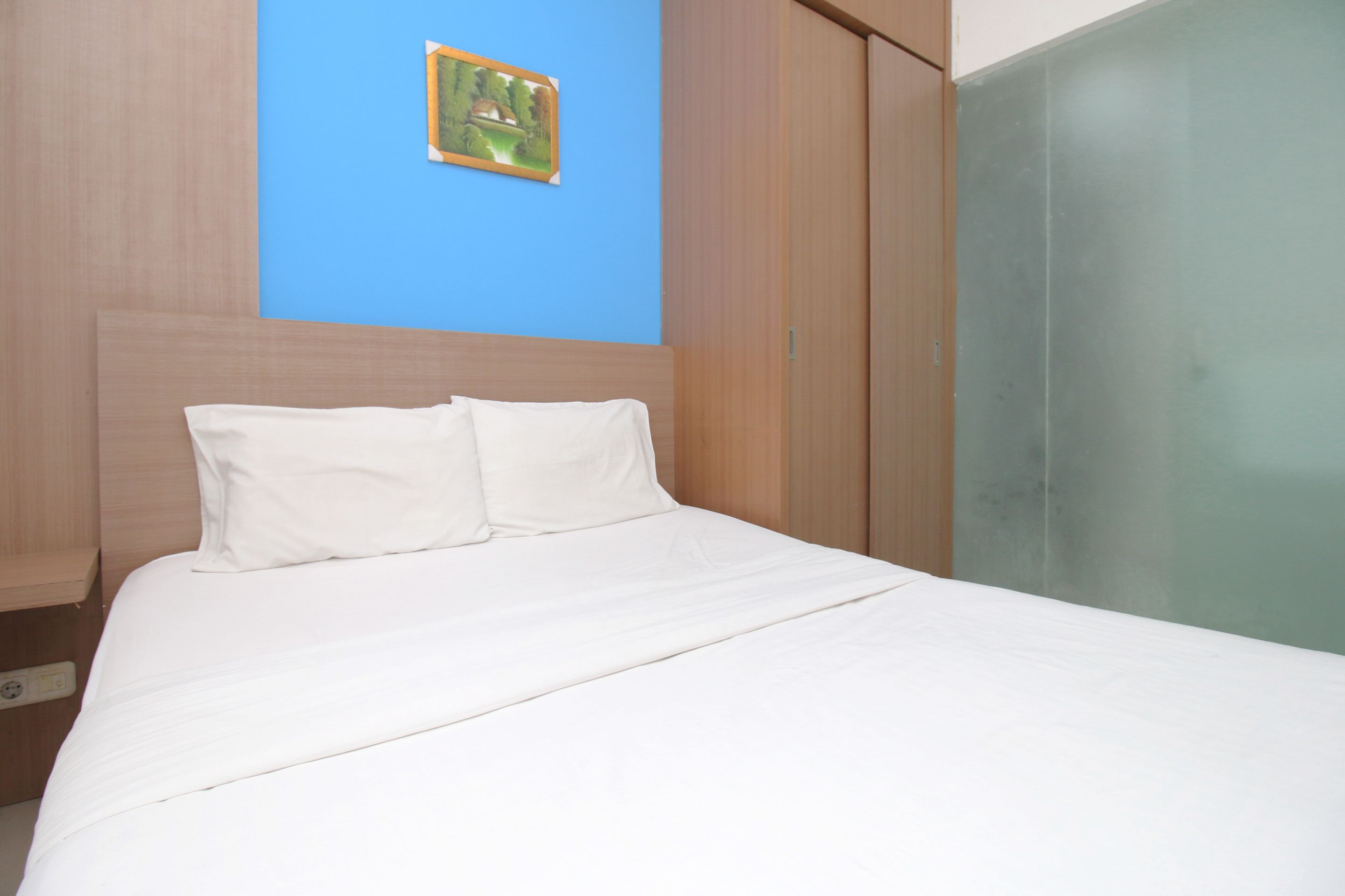 A neatly made bed with white linens in a room with a blue accent wall and a painting.