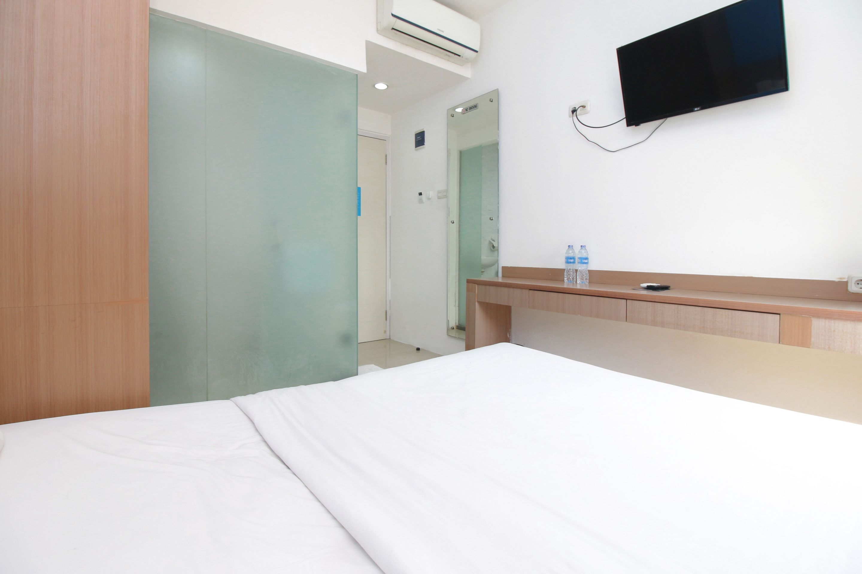 A hotel room with a bed, a wooden desk, a flat-screen TV, and a water bottle on the desk.