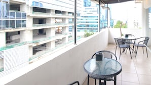 A balcony with a glass table and chairs, overlooking a construction site and modern buildings.