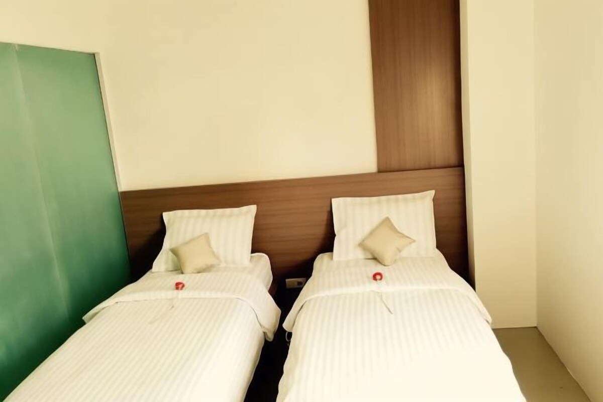 Two single beds with white bedding and beige pillows in a room with a wooden headboard and a green accent wall.