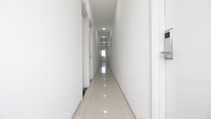 A long, narrow hallway with white walls and a shiny tiled floor, leading to a door at the end.