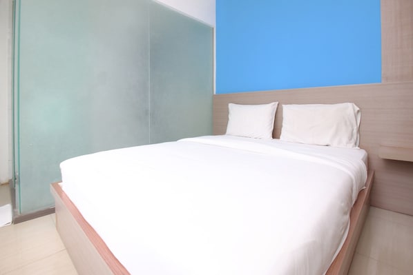 A neatly made bed with white linens in a modern room with a light wooden headboard and a blue accent wall. - Residence 100 (Jakarta)