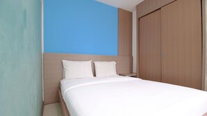 A neatly made bed with white linens in a room with a blue accent wall and a wooden wardrobe.