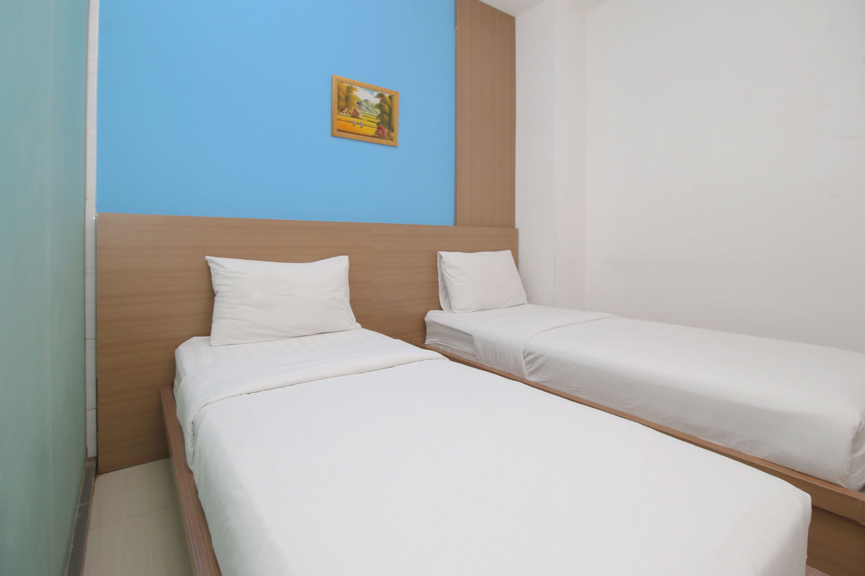A room with two single beds, a wooden headboard, a blue accent wall, and a small framed picture.