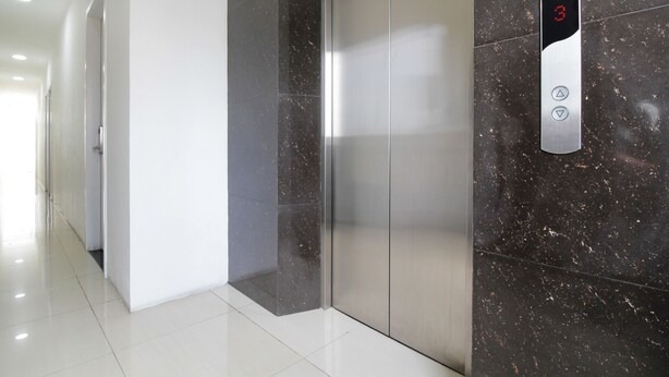 A modern elevator with a digital display showing the number 3, located in a hallway with white walls and a polished floor.