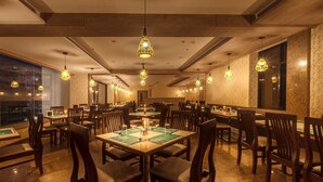 Un restaurant spacieux, doté de nombreuses tables et chaises, d’un éclairage suspendu et de grandes fenêtres offrant une vue sur la ville.