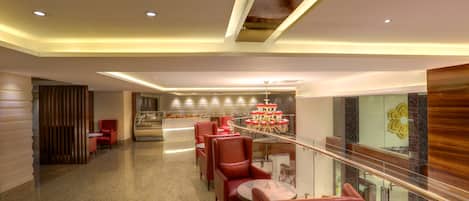 A modern hotel lobby with a glass railing, red leather seating, and a central table with a decorative centerpiece.