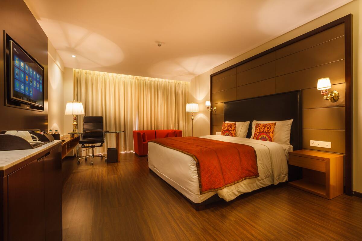 Een hotelkamer met een groot bed, een bureau met een computer, een televisie en een raam met gordijnen.