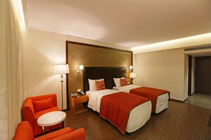 Habitación de hotel con dos camas, una mesita pequeña, dos sillas y una mesita de noche con lámpara.