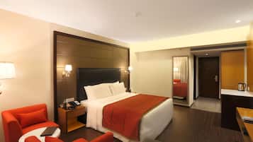 A hotel room with a bed, a desk, a chair, a nightstand, and a lamp.