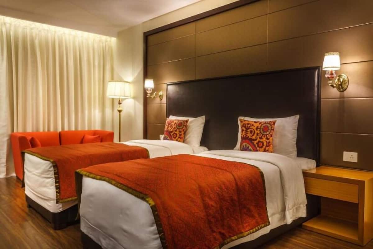 Een hotelkamer met twee bedden, een bank, een nachtkastje en een lamp.