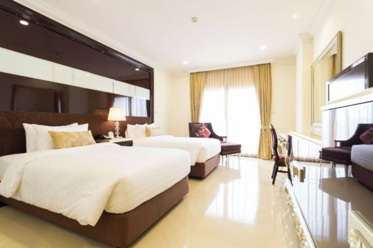 A hotel room with two beds, a sitting area with a chair, a TV, and a large mirror.