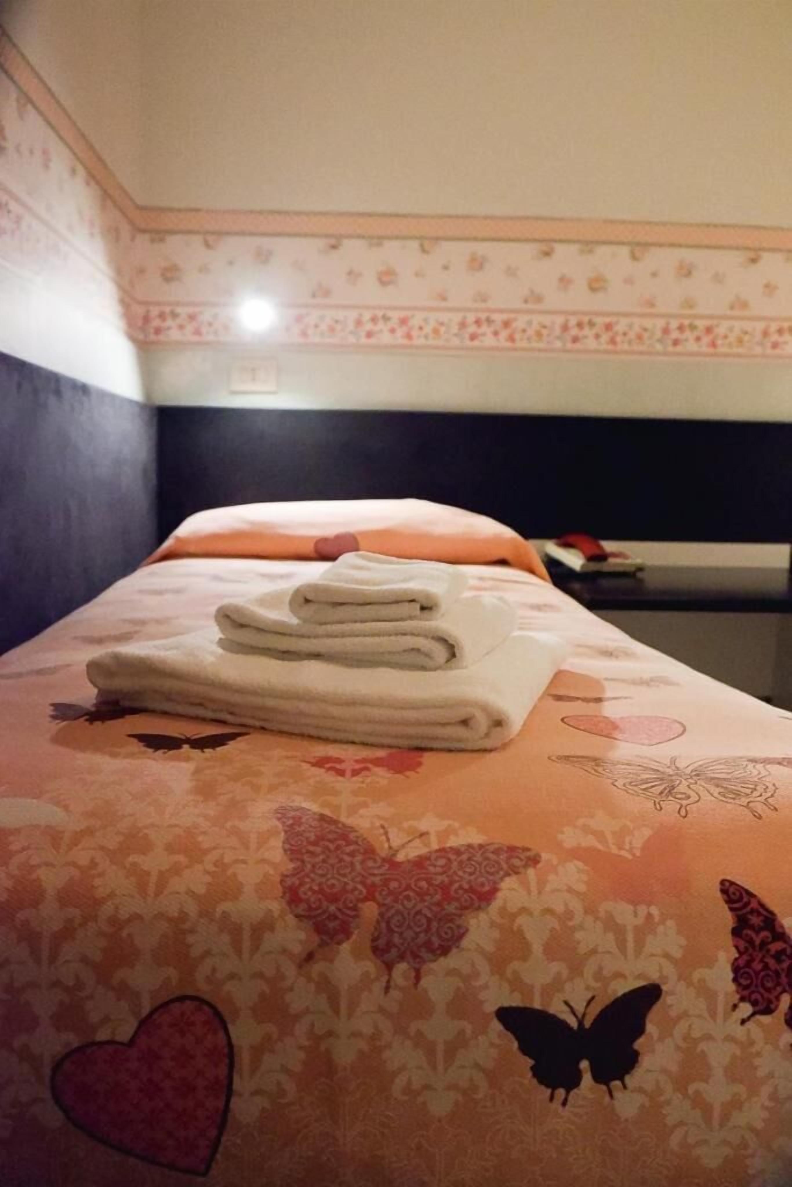 A neatly made bed with a floral-patterned bedspread and a folded white towel on top.