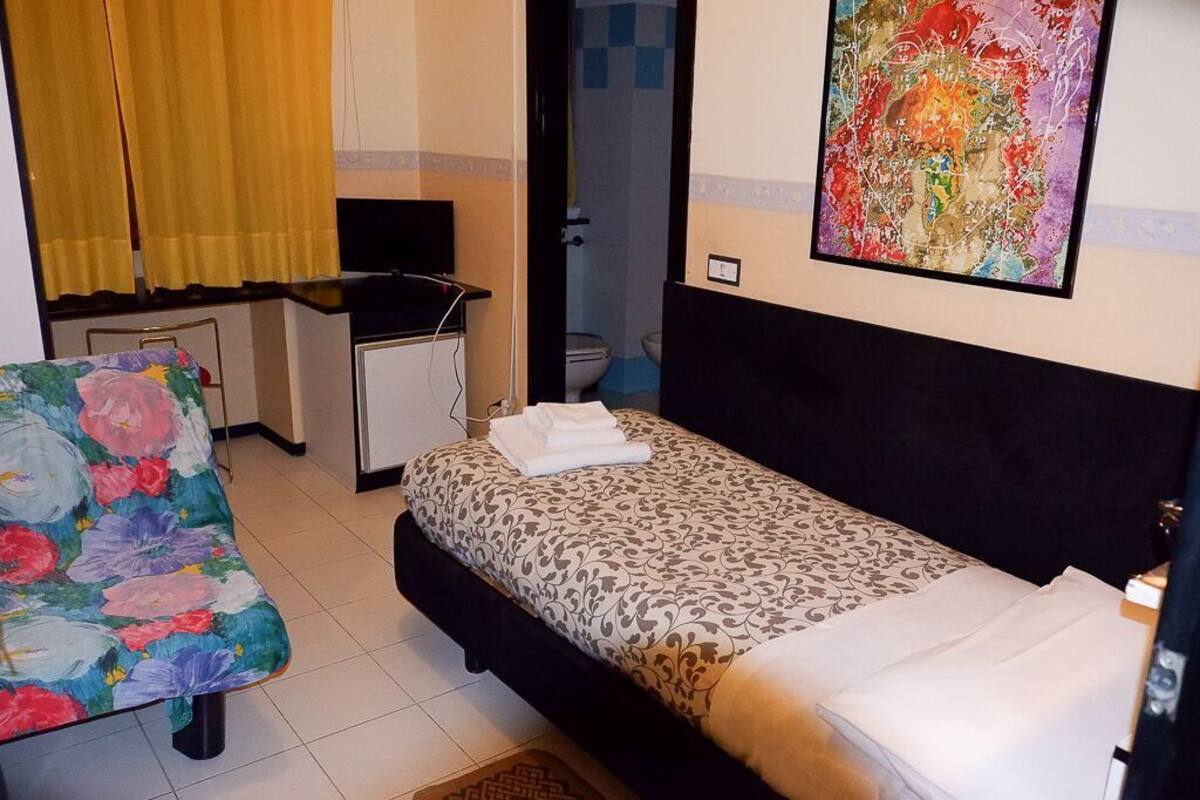 Une chambre à coucher avec un lit, un bureau, une chaise et une salle de bain visible à travers une porte ouverte.