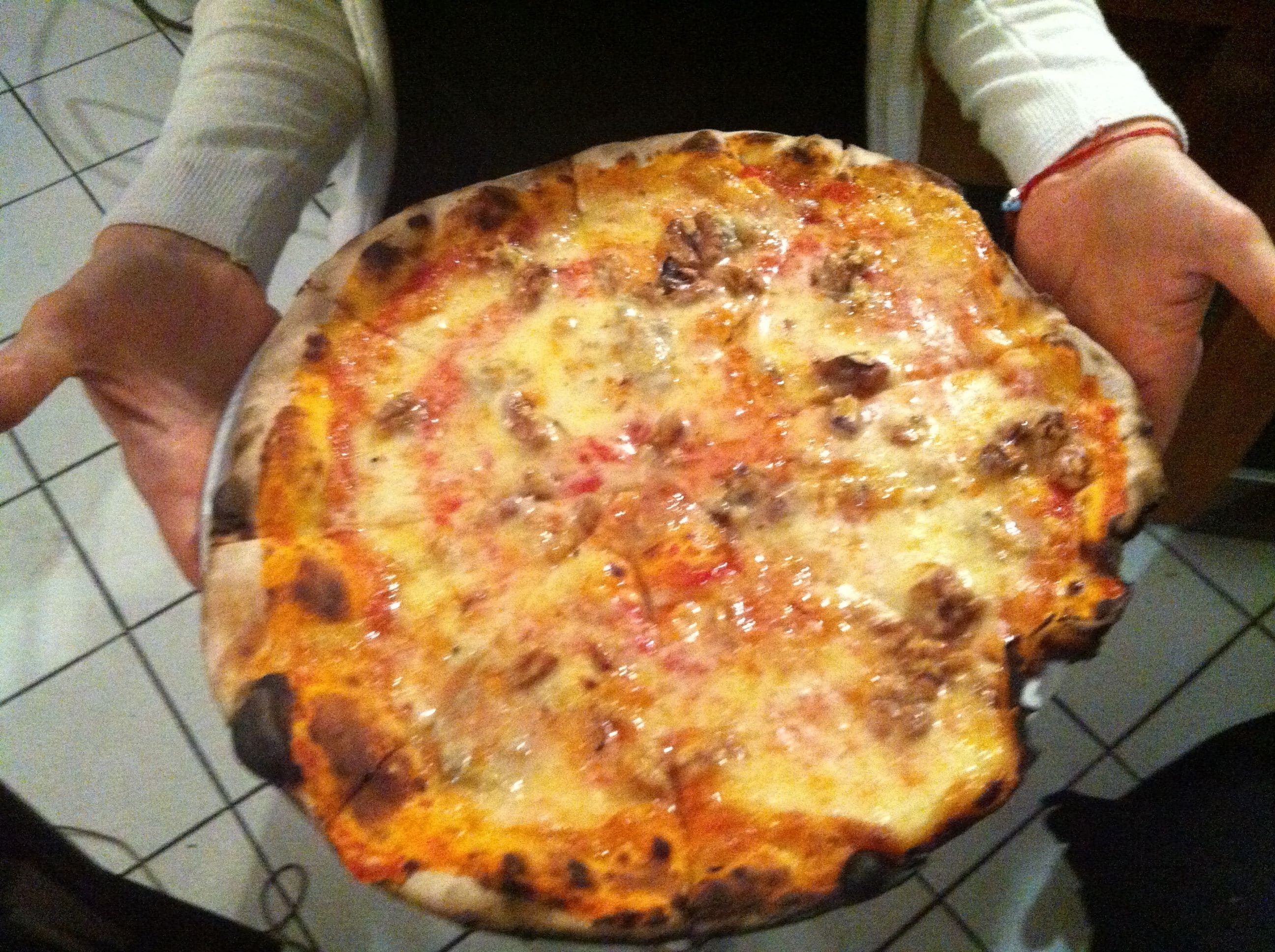 Una persona sosteniendo una pizza con ingredientes visibles.