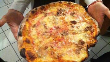 Una persona tiene in mano una pizza con condimenti ben visibili.