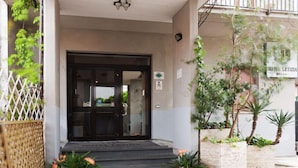 A hotel entrance with a glass door, a sign above the door, and potted plants on the steps. - Letizia Hotel (Orte)