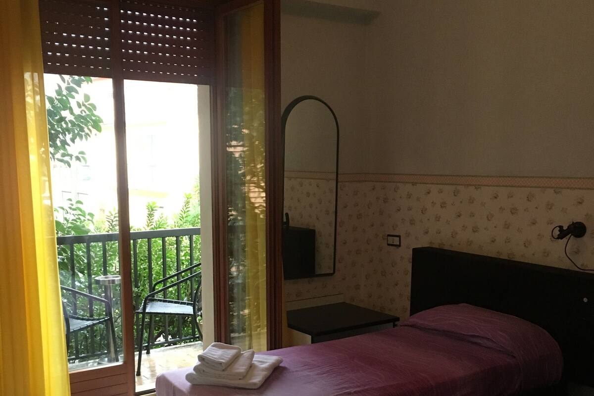 Une chambre d’hôtel avec deux lits, un balcon avec des chaises et une porte coulissante donnant sur l’extérieur.