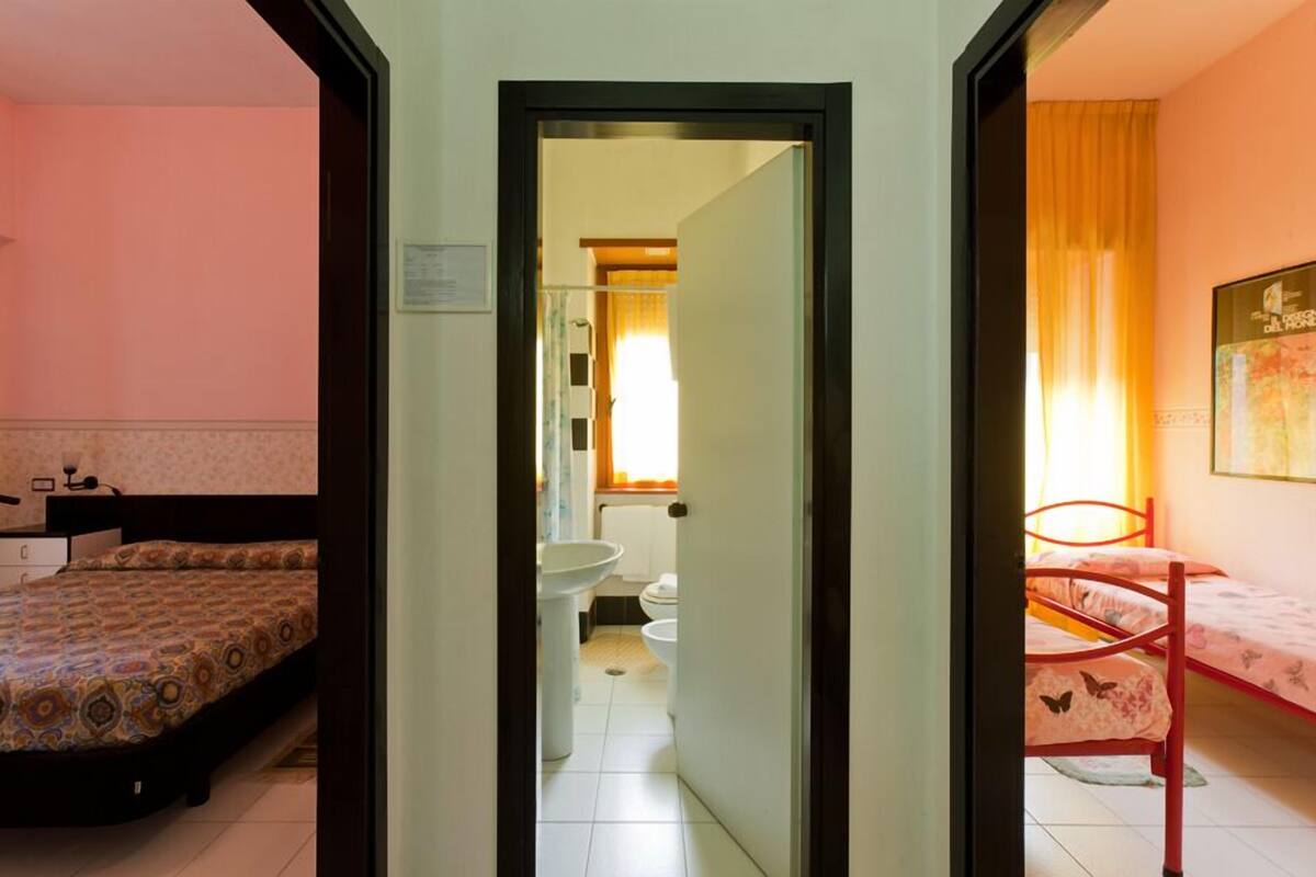 Une chambre d’hôtel comprenant un lit, une salle de bain avec des toilettes et un lavabo, et une porte donnant sur une autre pièce.
