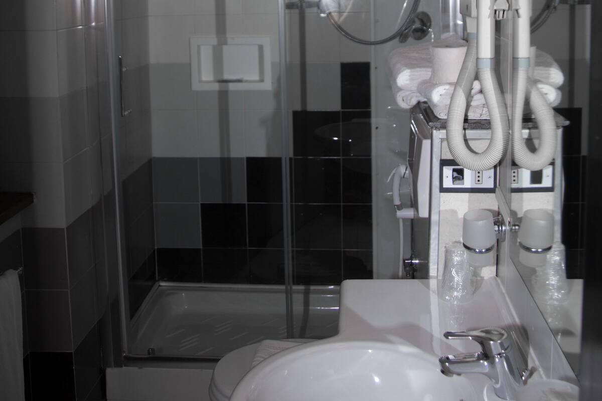 Une salle de bain moderne avec une douche à parois de verre, un lavabo blanc et un miroir agrémenté d’accessoires de toilette.
