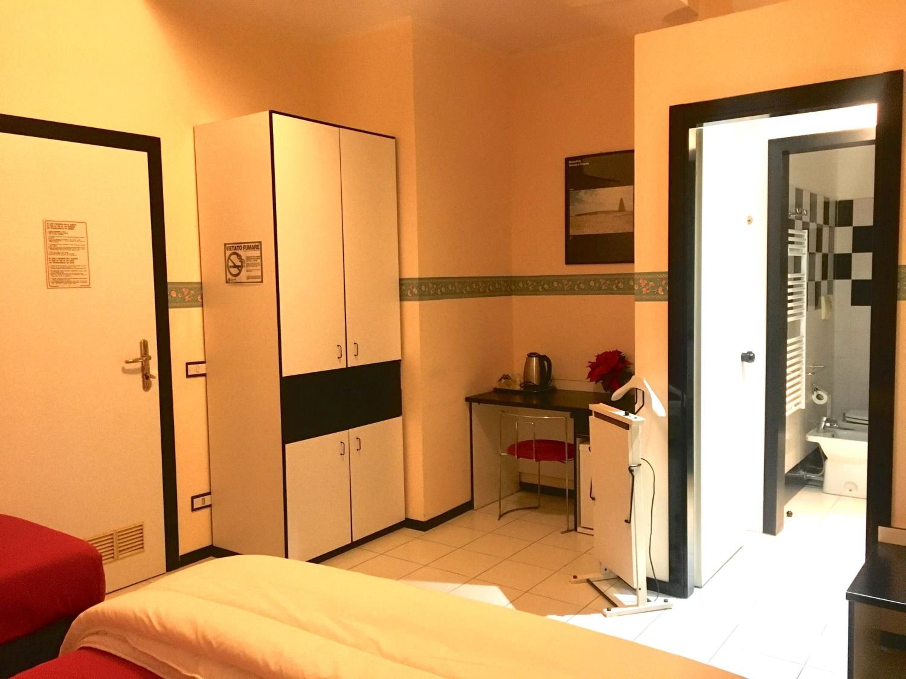 A hotel room with a bed, a desk, a kitchenette, and a bathroom.