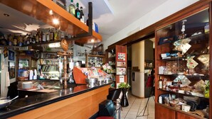 A bar area with a wooden counter, stools, and shelves stocked with bottles and glasses. - Letizia Hotel (Orte)