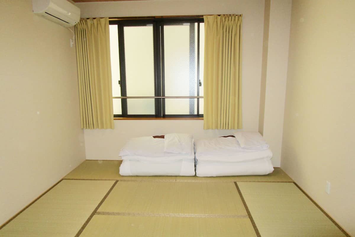 A room with a bed, a window with curtains, and an air conditioning unit.